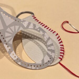 A template cut out of cardstock to mark baseball stitching and name and players number on a baseball keychain